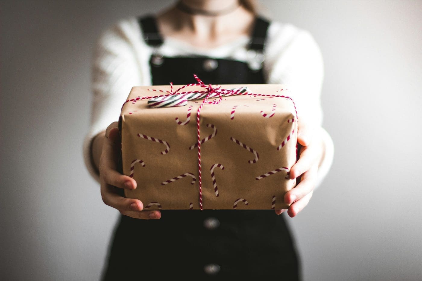 A person holds a brown paper gift with candy cane wrapping.