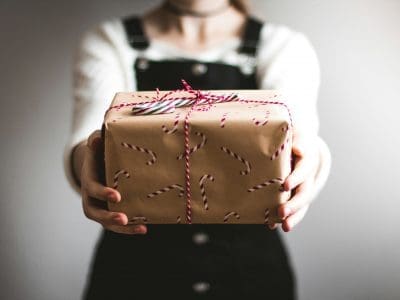 A person holds a brown paper gift with candy cane wrapping.