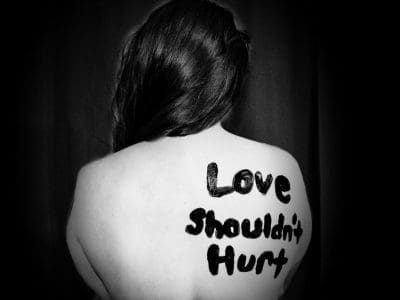 "Love Shouldn't Hurt" written in black on a woman's back.