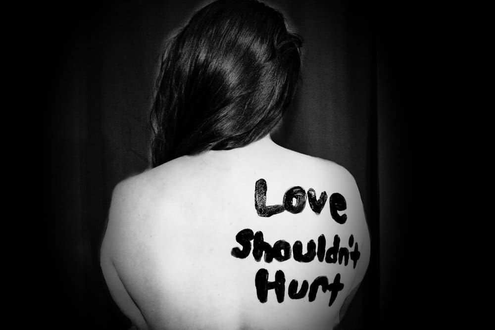 "Love Shouldn't Hurt" written in black on a woman's back.