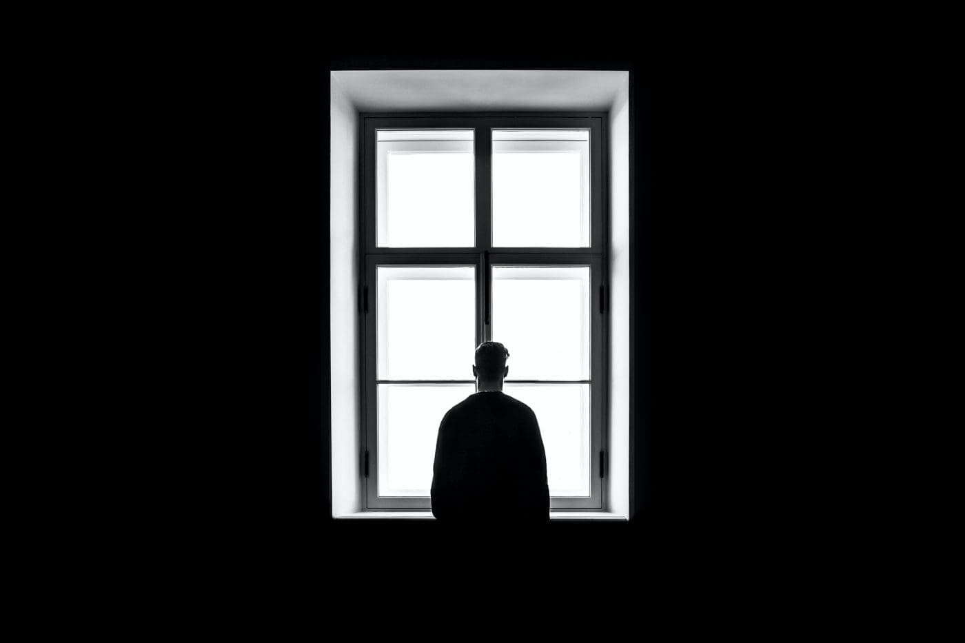 A silhouetted figure stands in front of a bright window.