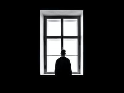 A silhouetted figure stands in front of a bright window.