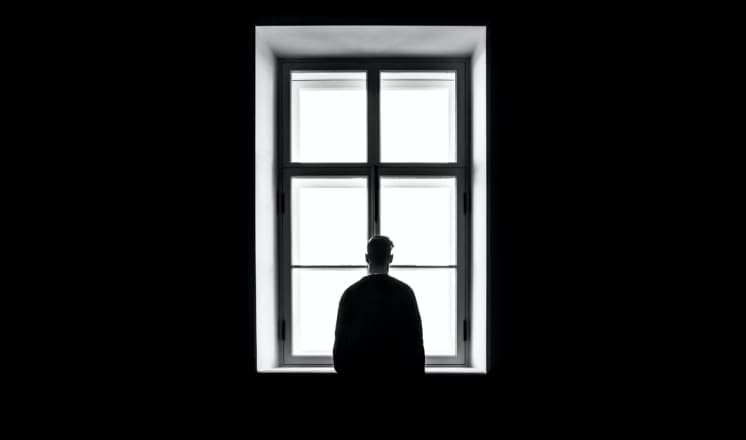 A silhouetted figure stands in front of a bright window.