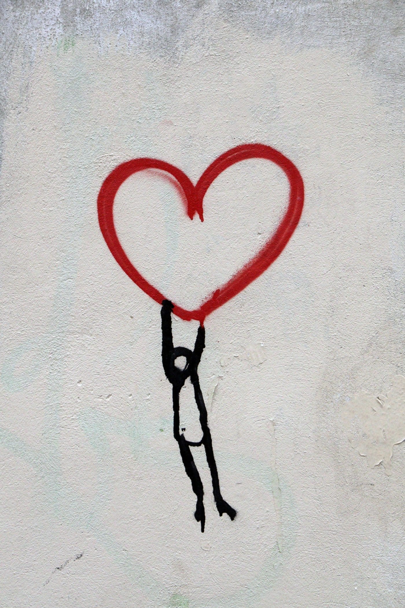 A black stick figure holds onto a large red heart, a graffiti painting.