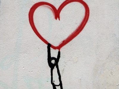 A black stick figure holds onto a large red heart, a graffiti painting.