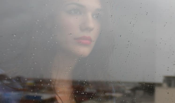 A woman with pink lipstick looks out a rain-streaked window.