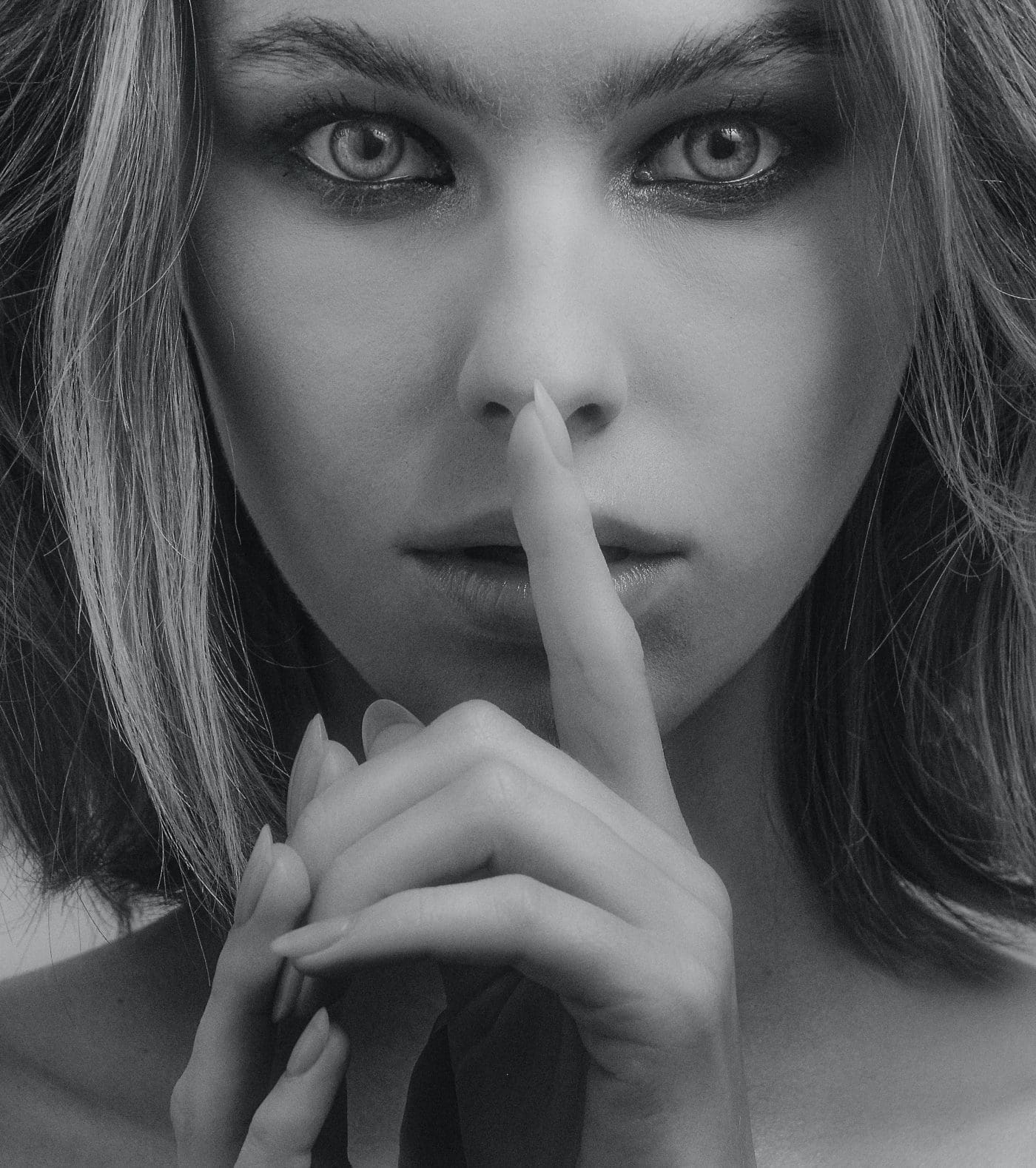 A black and white photo of a person with a finger to their lips.