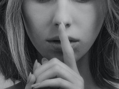 A black and white photo of a person with a finger to their lips.