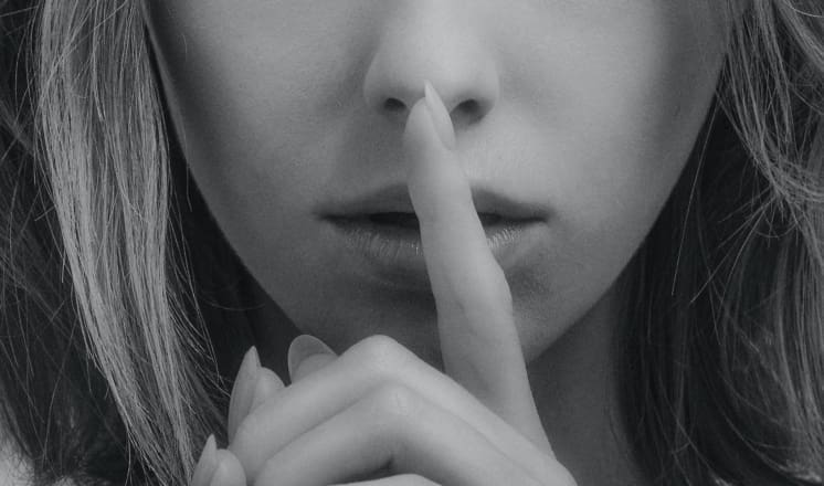 A black and white photo of a person with a finger to their lips.