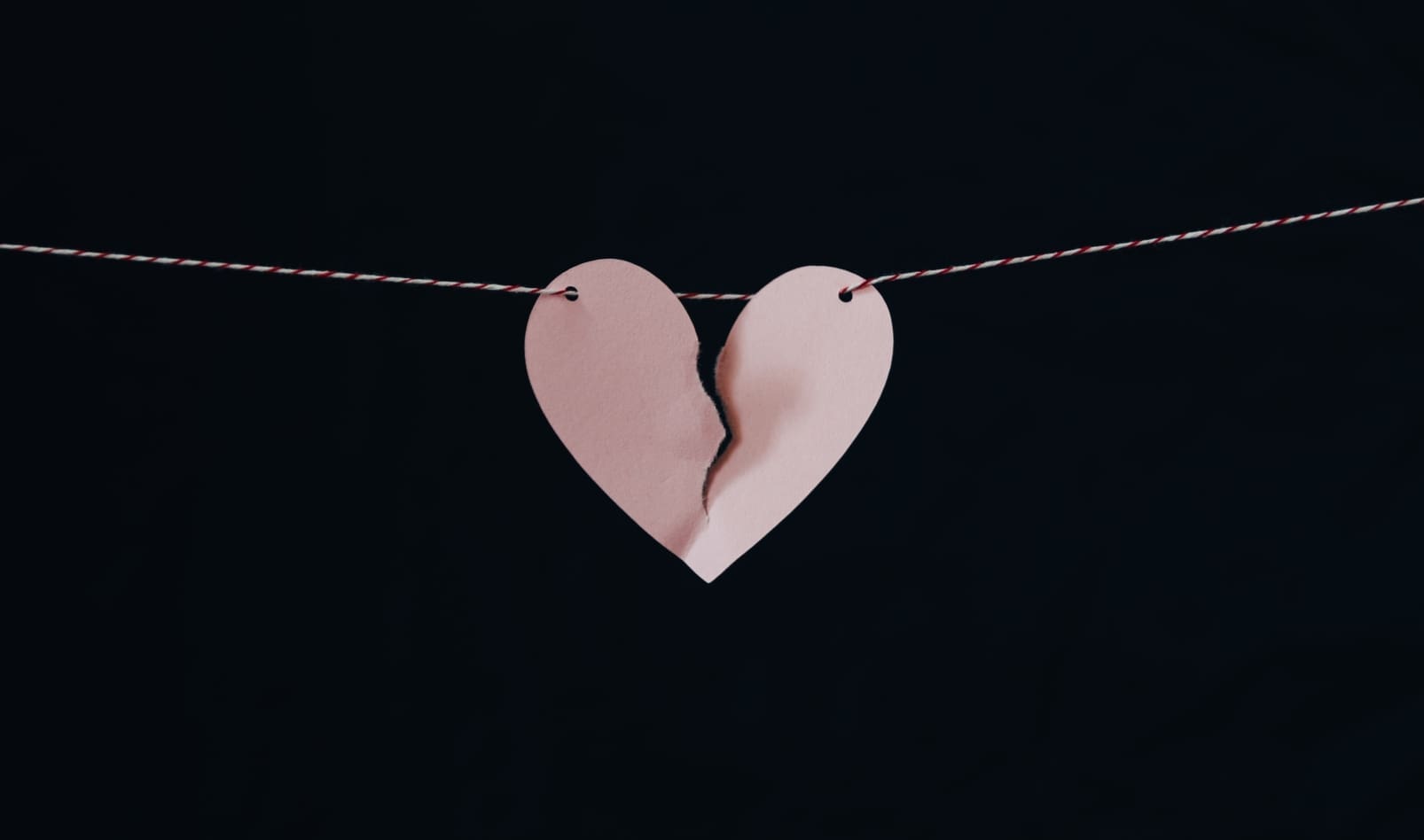A pink paper heart is torn in half and hanging on a string.