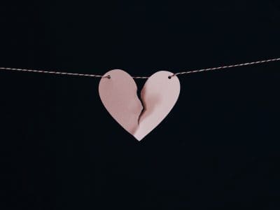 A pink paper heart is torn in half and hanging on a string.