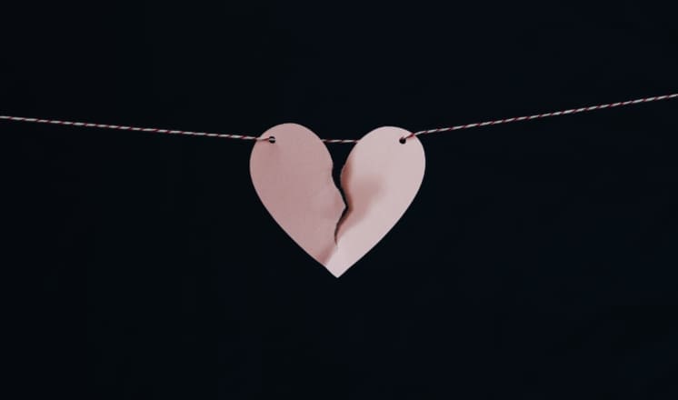A pink paper heart is torn in half and hanging on a string.