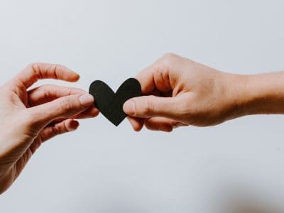 Two hands pass a small black heart made of paper.