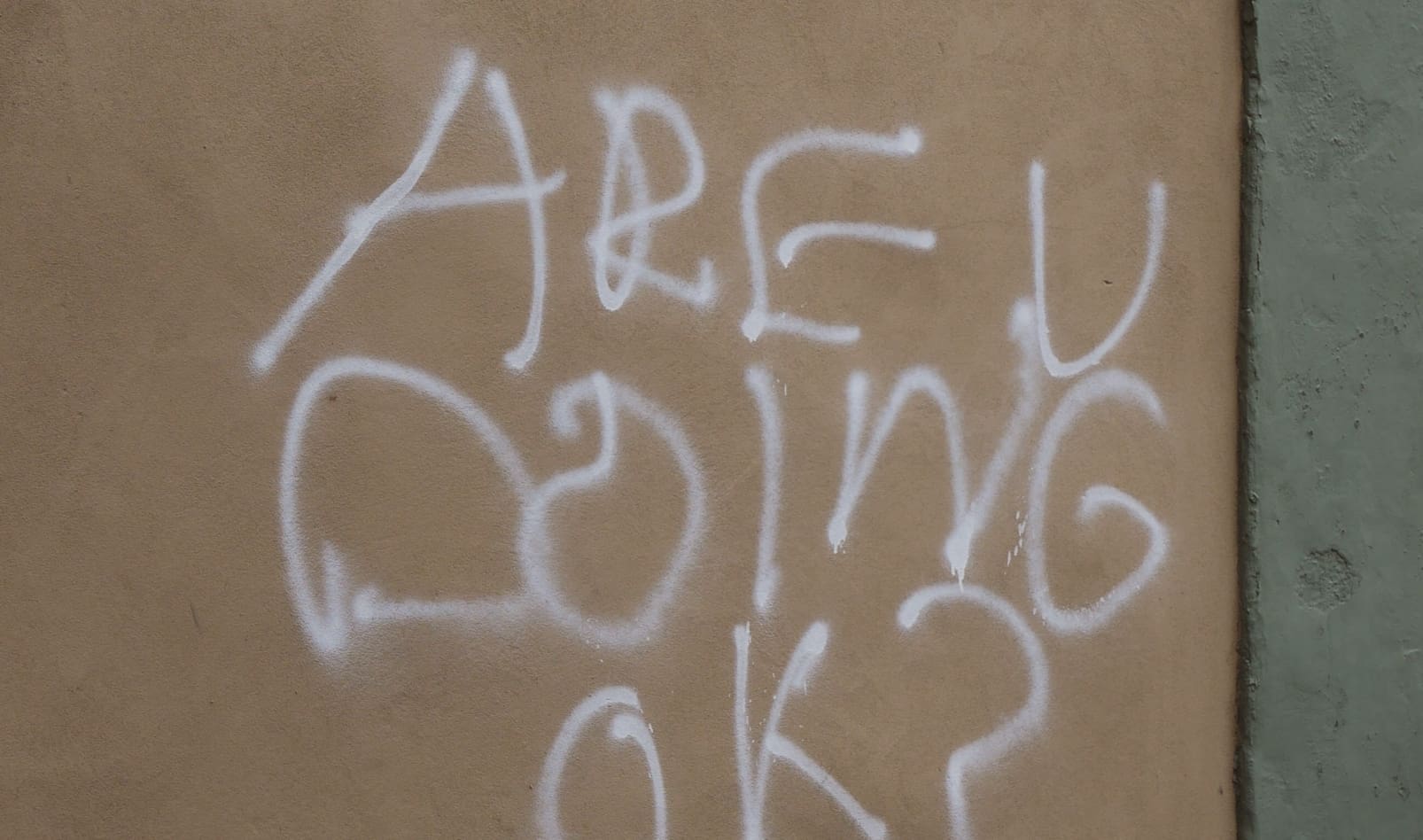 "ARE U DOING OK?" is spray-painted on a tan wall.