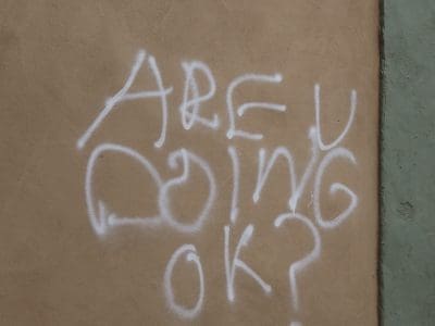 "ARE U DOING OK?" is spray-painted on a tan wall.