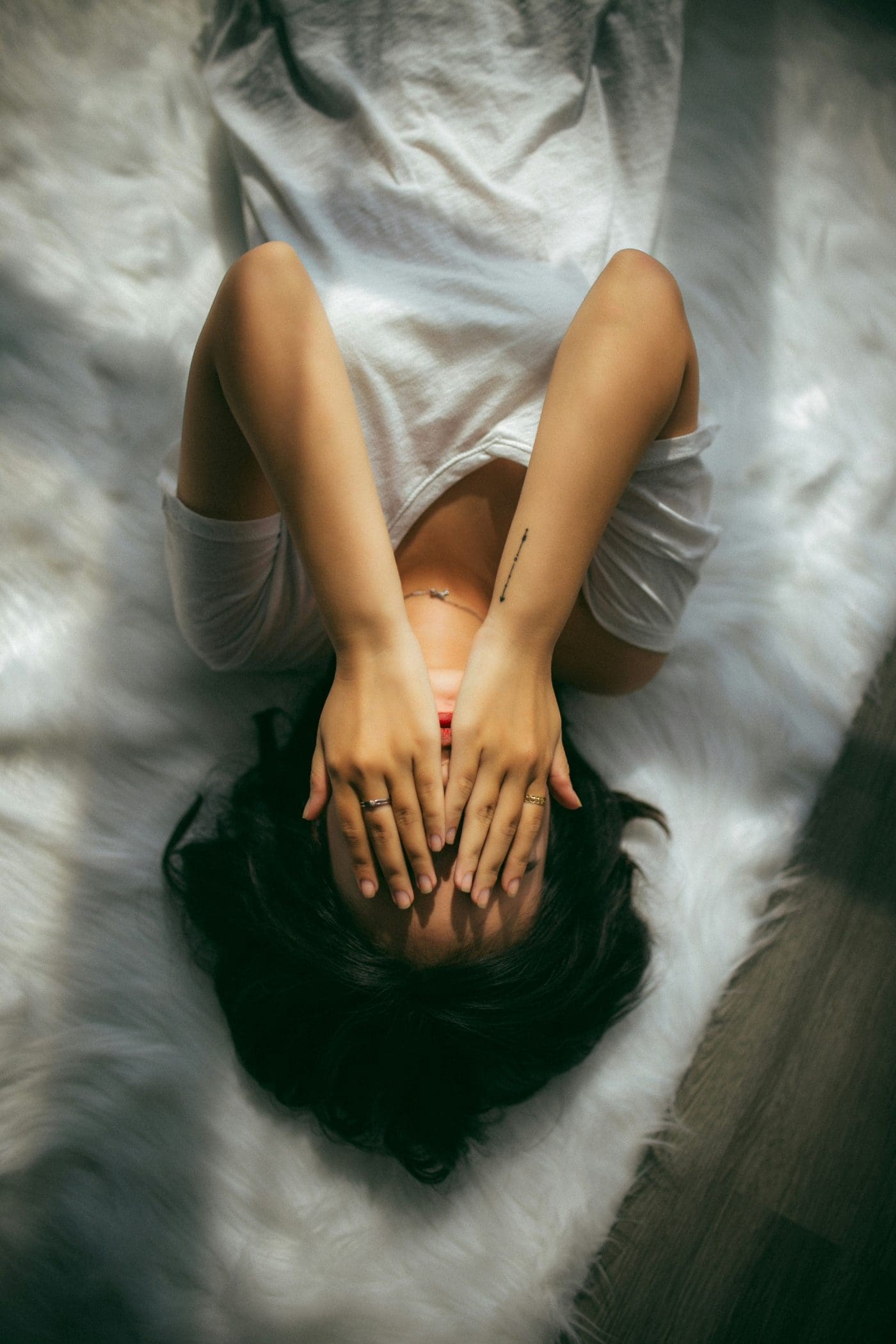 A person lies on their back, covering their face with their hands.