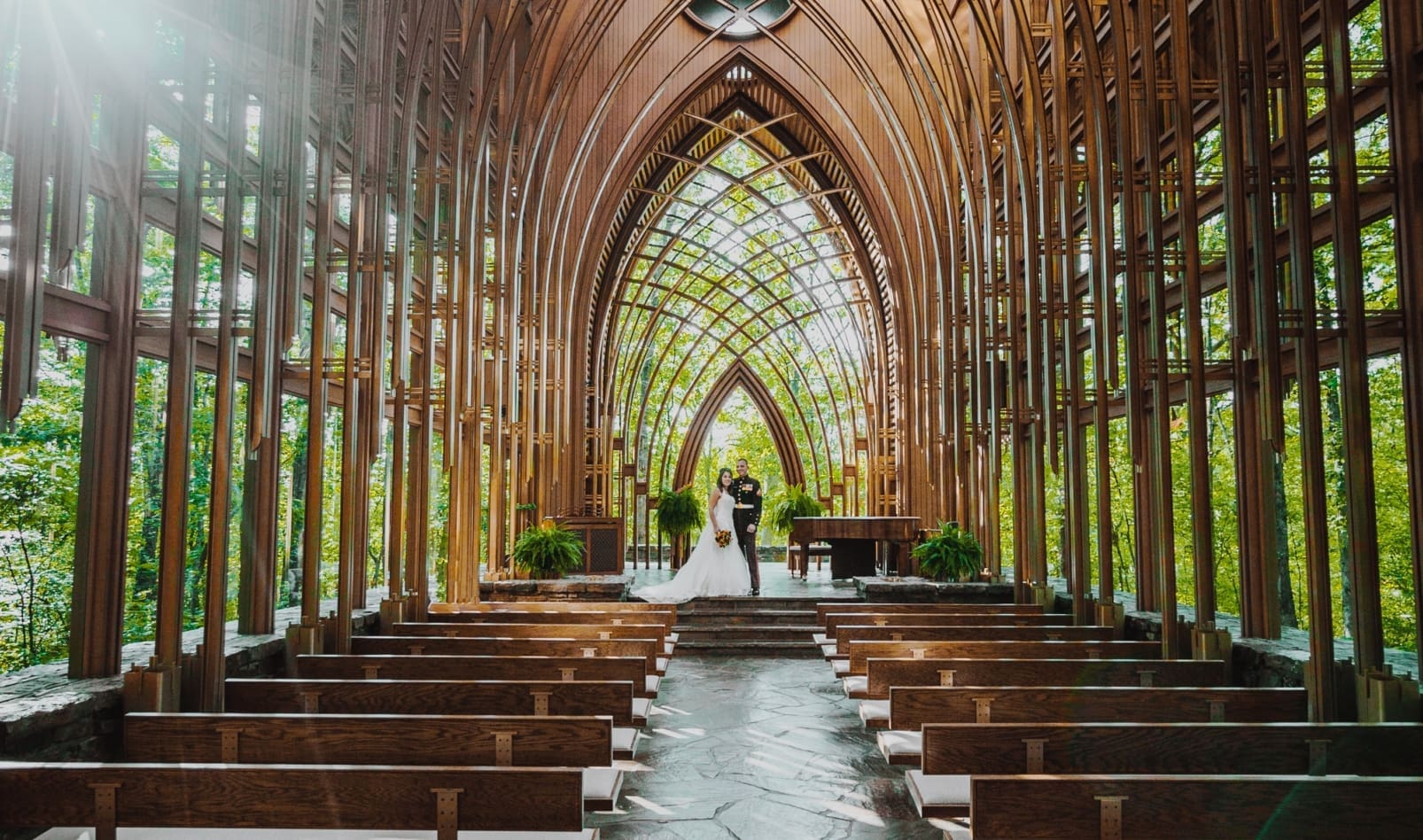 A newlywed couple kisses at the end of a wooden church aisle.