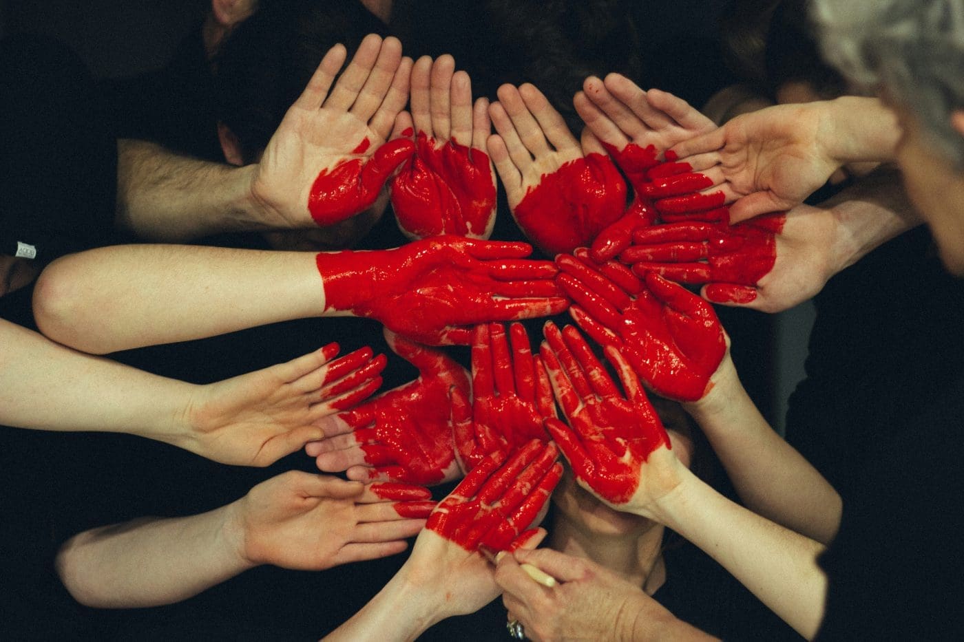 A circle of people with their hands painted red, reaching in.