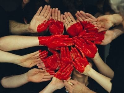 A circle of people with their hands painted red, reaching in.