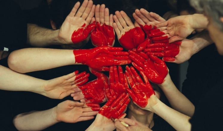 A circle of people with their hands painted red, reaching in.